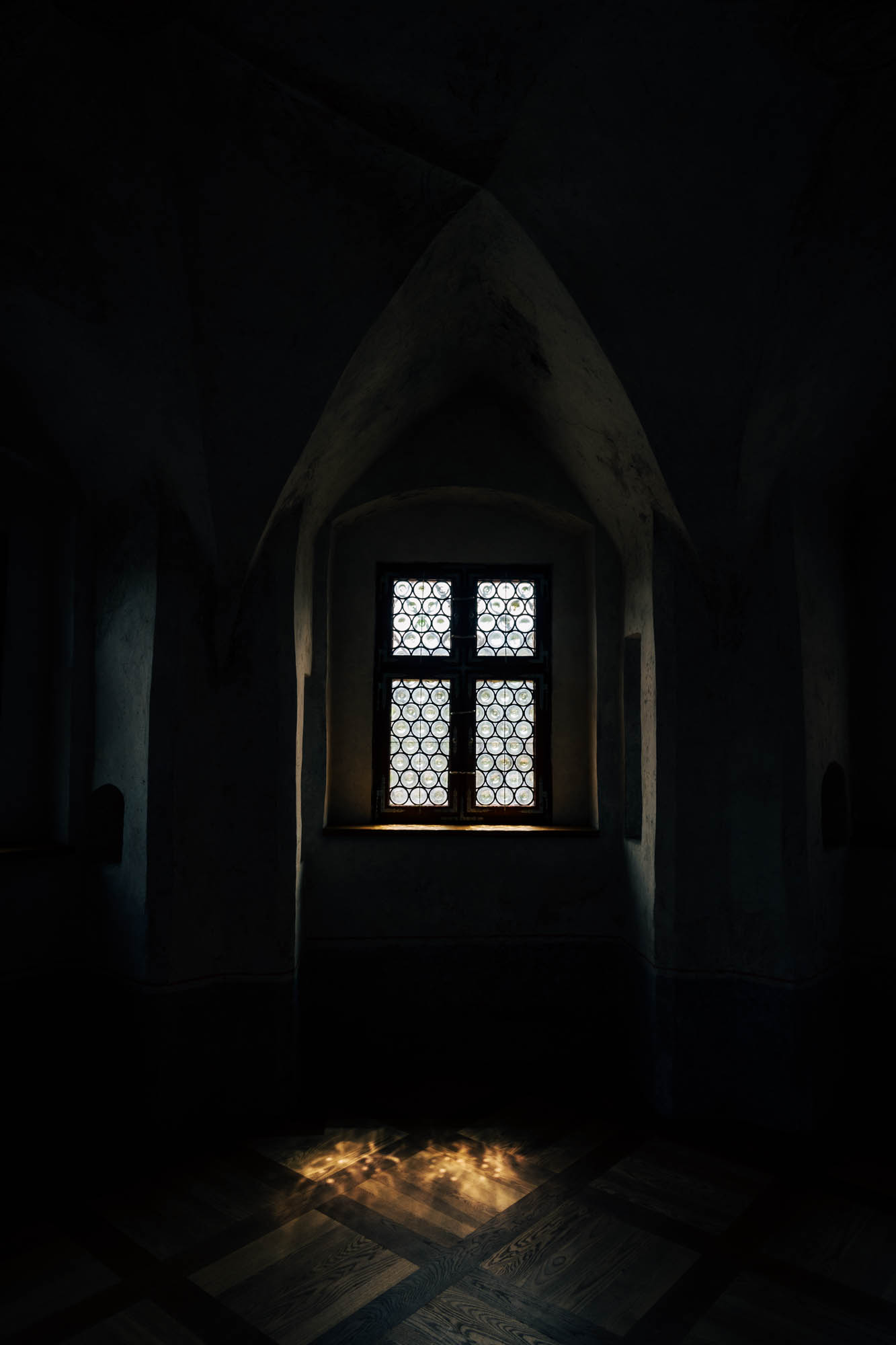 Ein Fenster und eine Lichtpfütze auf dem Boden. Bemerkenswert ist das Gitter aus Metallringen, die durch Bienenwaben verbunden sind.