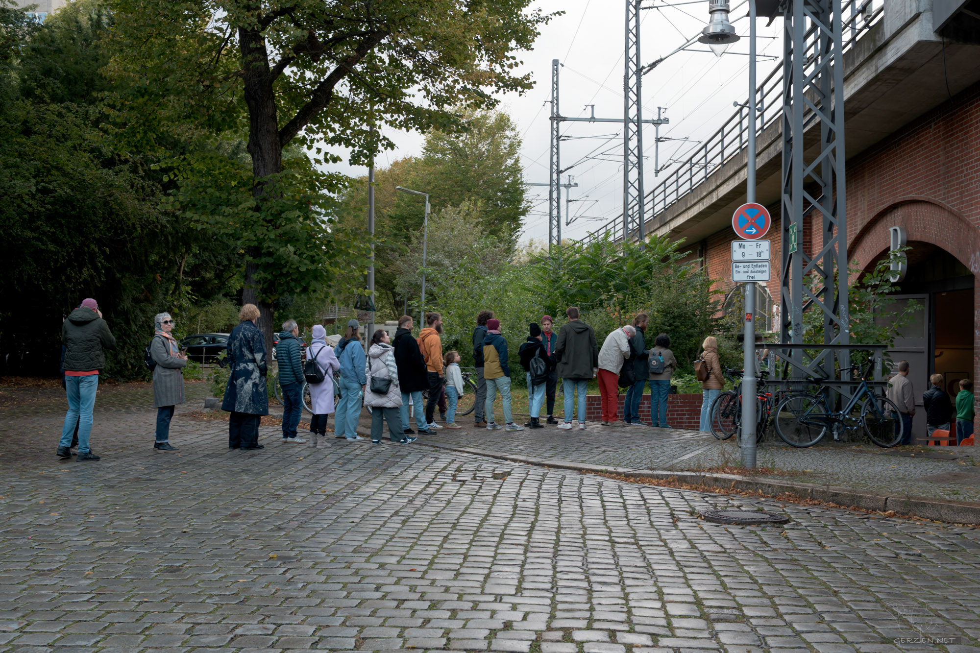 Vor dem Eingang steht eine lange Warteschlange, die bis auf die Straße reicht. Immer wieder kommen weitere Menschen dazu.